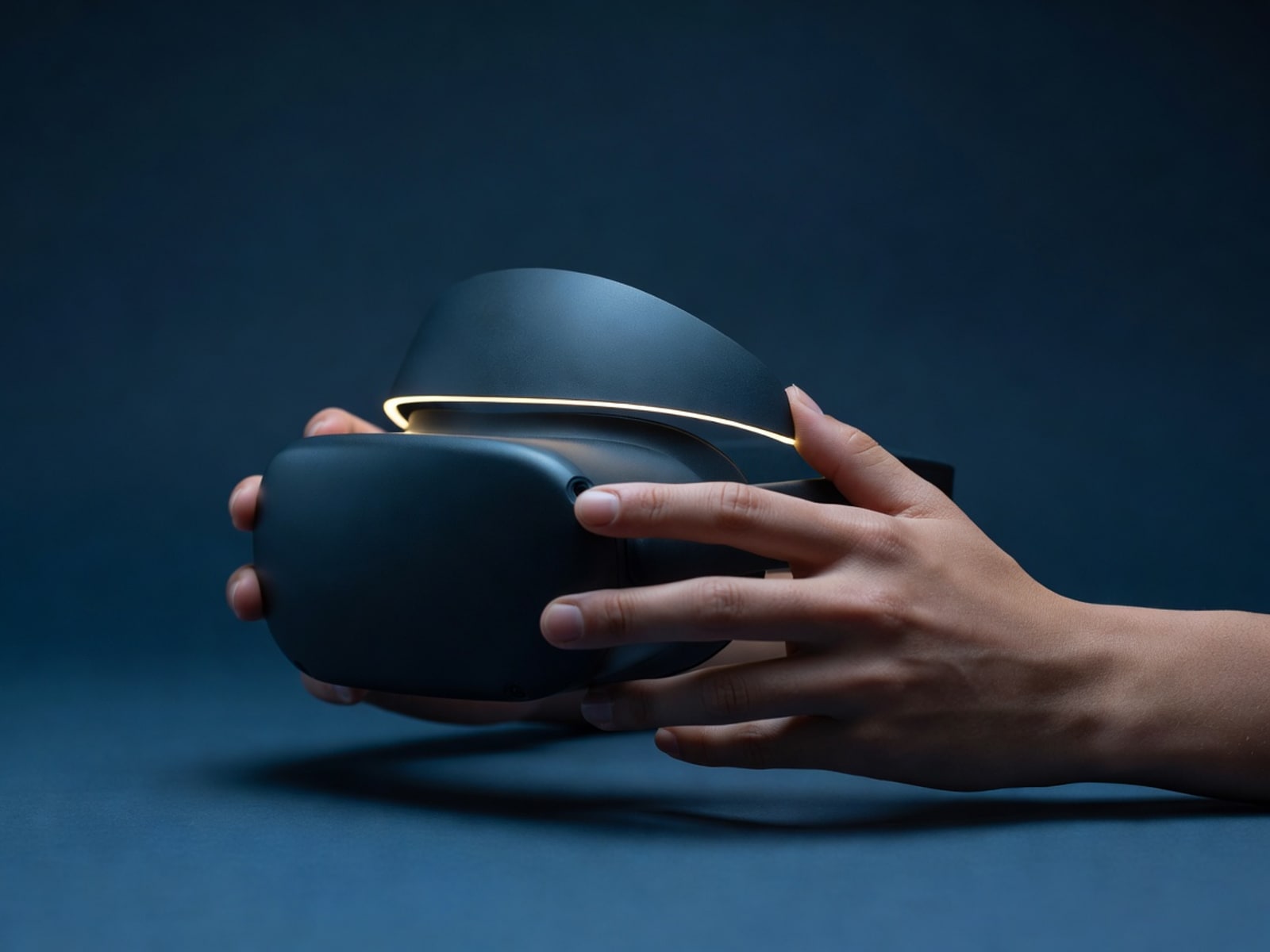 Hands holding a Meta Quest headset against a deep navy backdrop with a warm amber rim light.